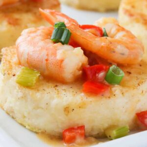 A platter of grit cakes topped with sauce and shrimp