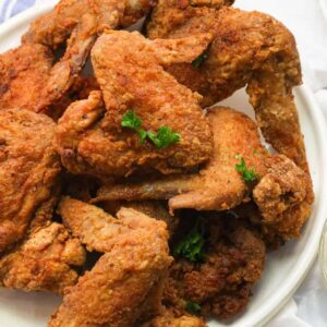 A plate piled high with fried chicken wings and hot sauce and remoulade on the side