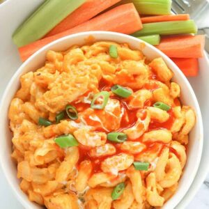 A tempting bowl of Buffalo Chicken Mac and Cheese drizzled with blue cheese dressing and hot sauce with celery and carrot sticks on the side