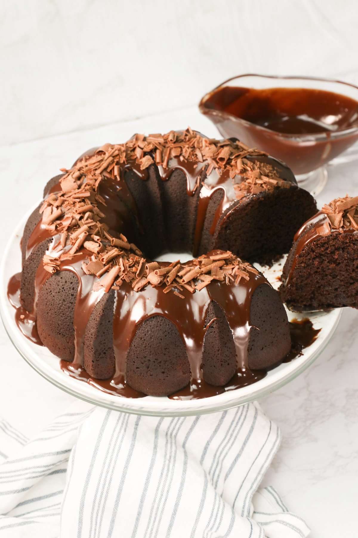 Slicing into an insanely decadent chocolate bundt cake with chocolate ganache drizzled over it and sprinkled with chocolate shavings