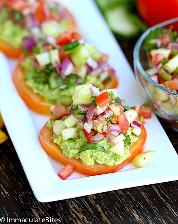 A white platter lined with tomato slices topped with avocado and kachumbari for a healthy and delicious snack