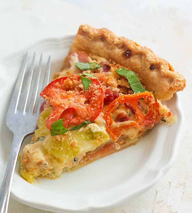 Serving up a slice of savory tomato pie on a white plate.