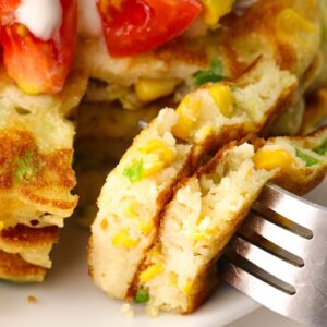 Taking a delicious bite out of a stack of corn cakes topped with sour cream, tomatoes, corn, and avocadoes