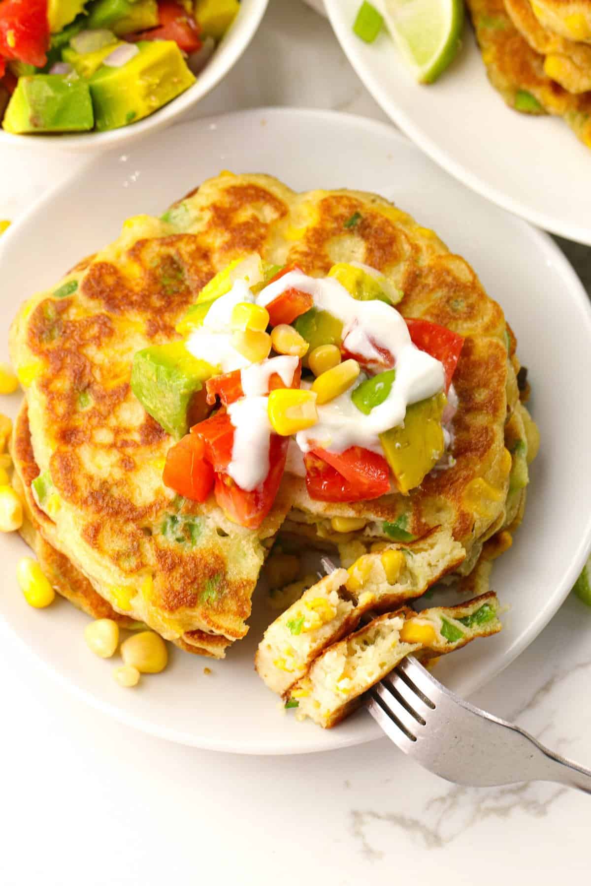 Enjoying a plateful of corn cakes topped with tomatoes, sour cream, avocados, and fresh corn