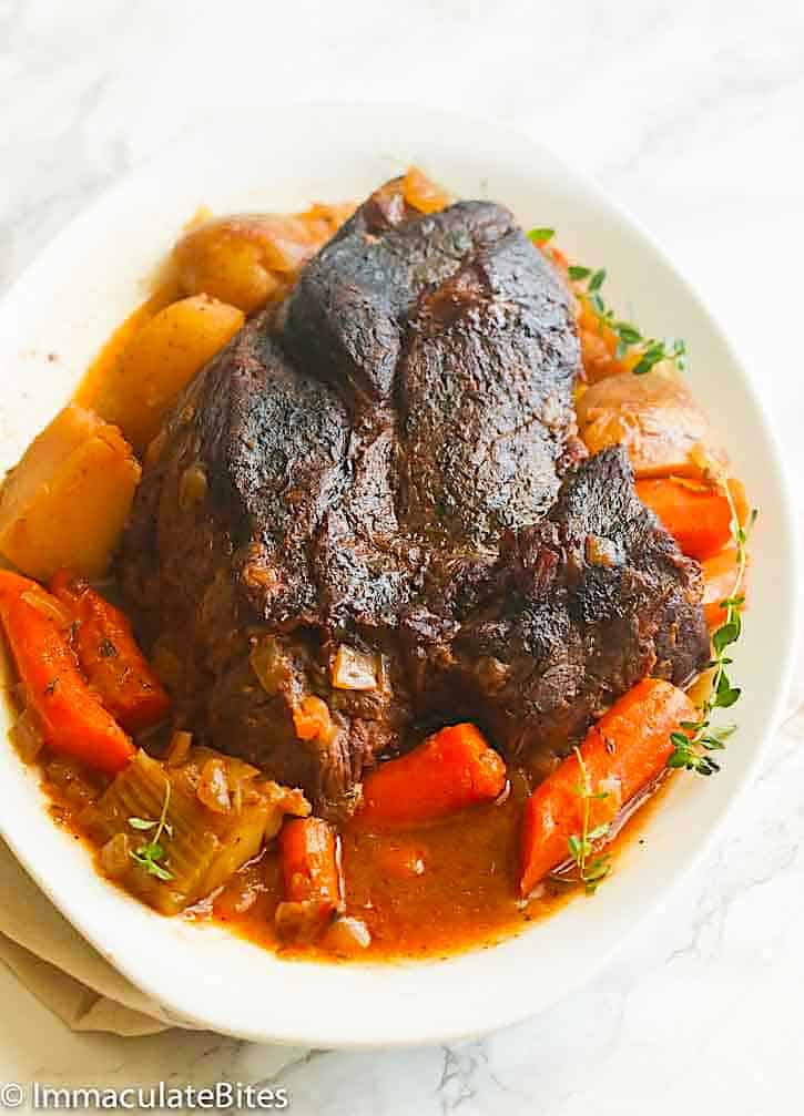 Serving up slow cooker pot roast on a white platter surrounded by delicious carrots and potatoes