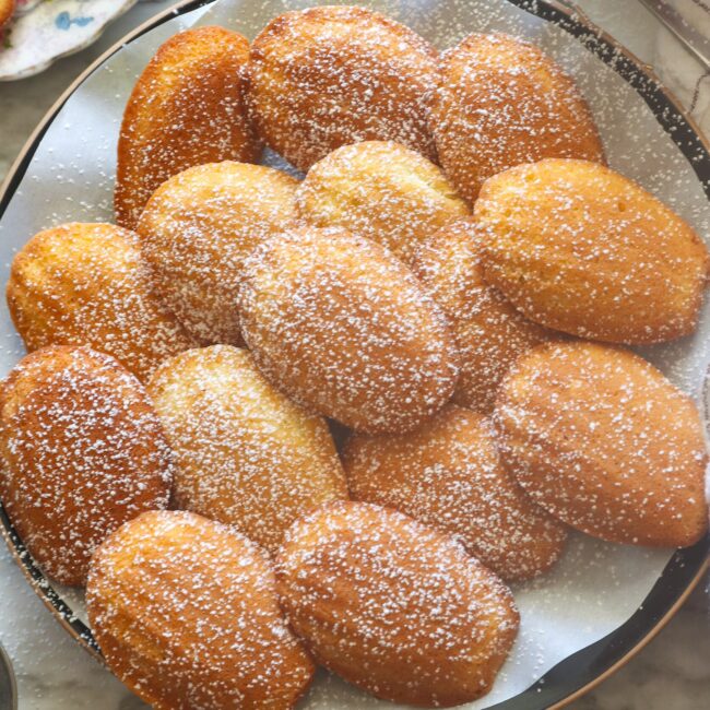 Freshly baked madeleine cookies dusted with powdered sugar ready to enjoy