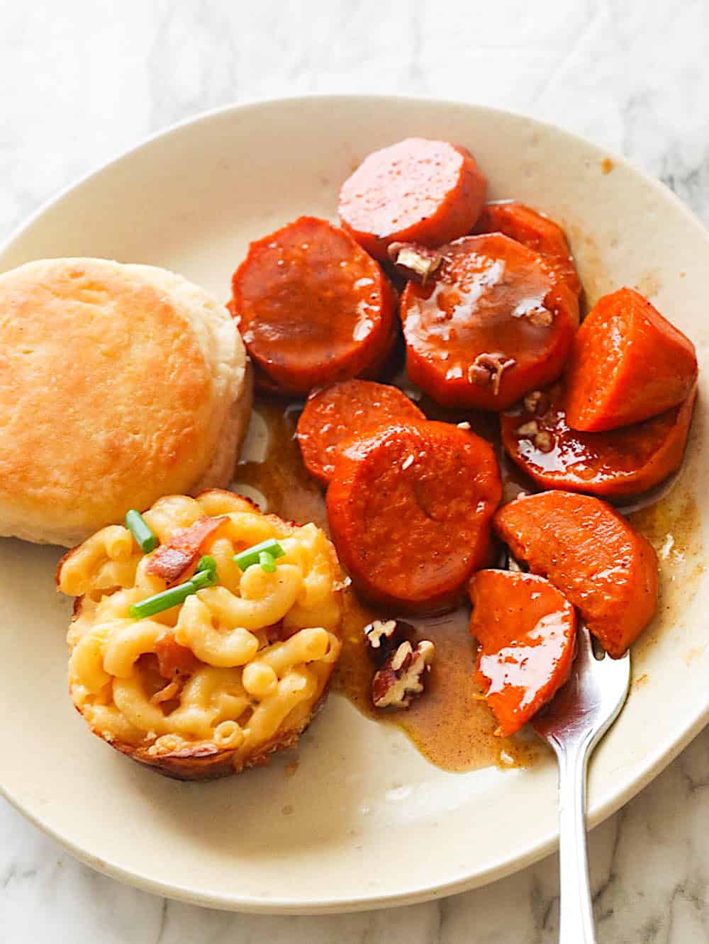 Candied yams and a hot out of the oven biscuit decorate the plate with a mac and cheese bite