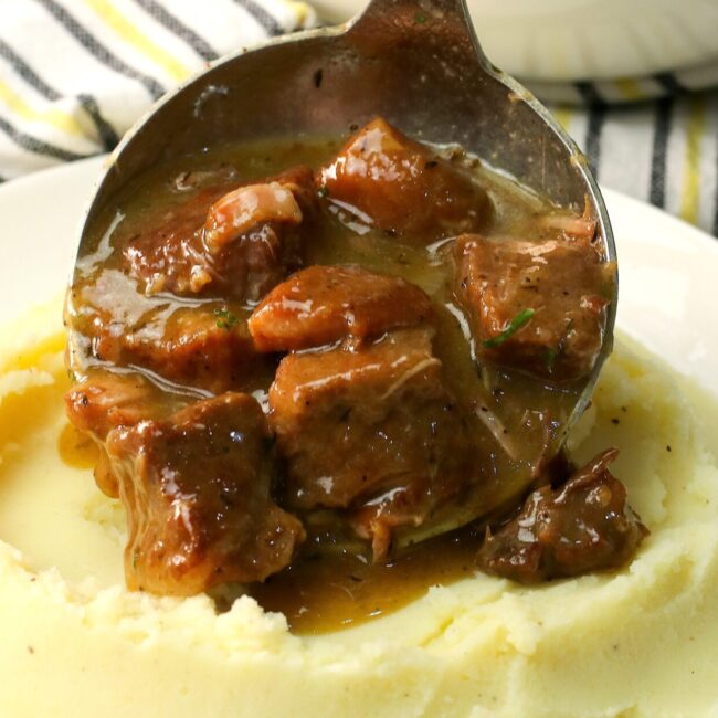 Serving fork-tender slow cooker beef tips over creamy mashed potatoes