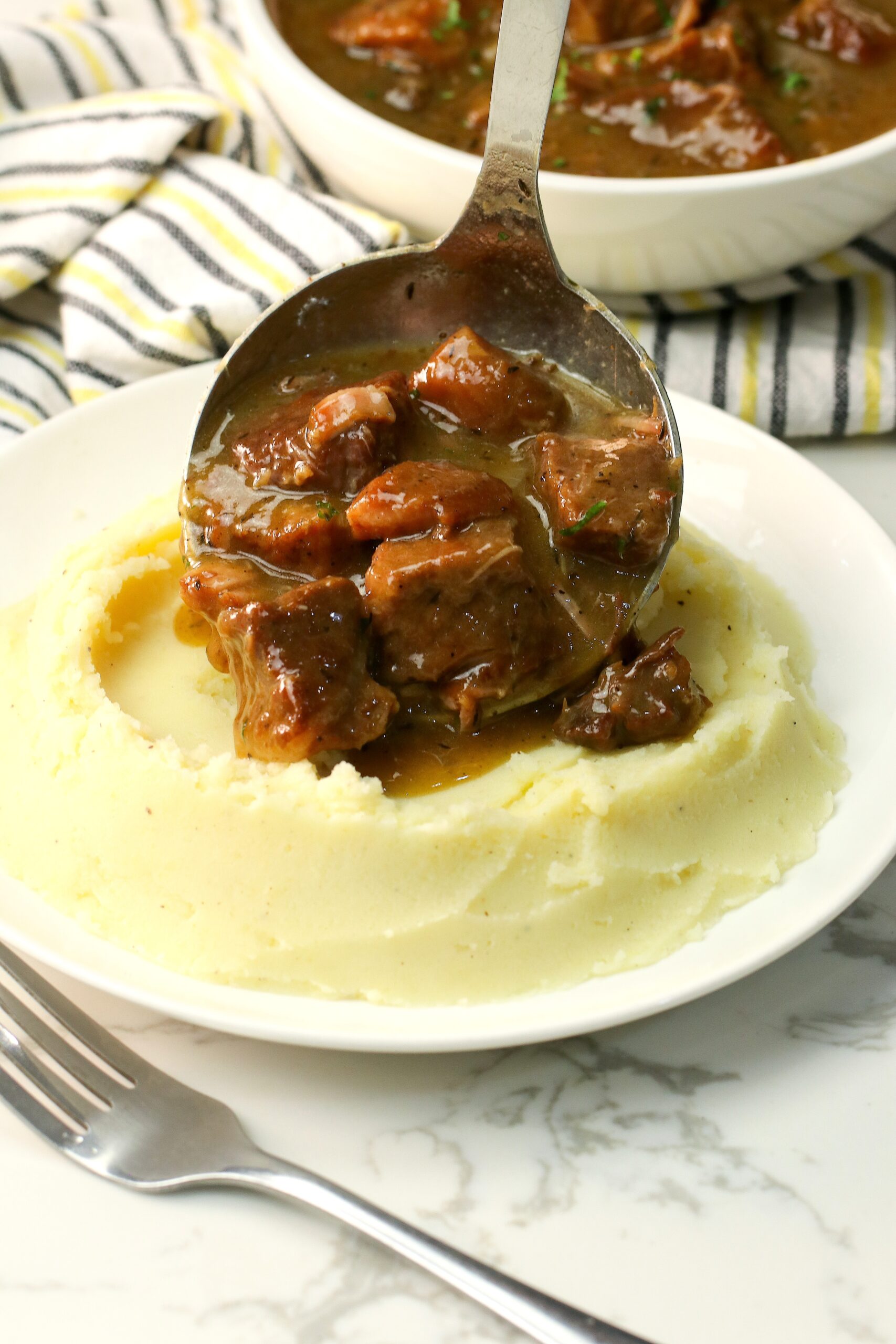 Serving fork-tender slow cooker beef tips over creamy mashed potatoes